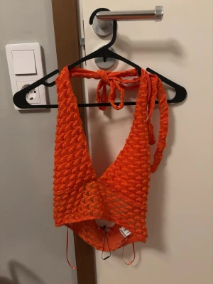 Orange virkad halterneck topp - Snygg orange virkad halterneck topp med djup v-ringning och knyt i nacken. Toppen har ett unikt strukturmönster och är croppad, perfekt för sommarens alla tillfällen. Materialet känns luftigt och lätt. Från Bershka i storlek S. Superfin med har inte kommit till användning för min del. Helt ny och aldrig använd.🧡 man kan knyta hur hårt eller löst man vill ha den. Helt slutsåld på nätet, ordinarie pris 230.