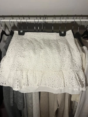 Vit spetskjol med volang - Söt vit kortkjol i spets med volangkant nedtill. Kjolen har en dragkedja på sidan och har en ganska tajt passform.