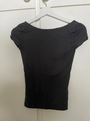 Svart croppad topp med öppen rygg - Snygg svart croppad topp med korta ärmar och djup, öppen rygg. Tight passform och enkel design som passar perfekt till jeans eller kjol. Tillverkad i mjukt material som känns skönt mot huden.