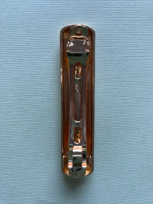 Guldig metallisk hårklämma - Snygg hårklämma i metall med en blank, guldig finish och avlång, rundad form. Perfekt för att hålla håret på plats och ge en stilren touch till din look. Klämman har en enkel och modern design utan dekorationer.