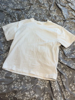 Vit t-shirt från 157, XS - En enkel och stilren vit t-shirt från 157 i storlek XS. T-shirten har klassisk passform med korta ärmar och rund halsringning. Perfekt för att matcha med jeans eller shorts. Materialet känns mjukt och bekvämt, troligtvis bomull.