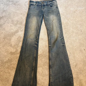 Blå bootcut jeans från Bershka - Säljer ett par blå bootcut jeans från Bershka i storlek 34. Jeansen har klassisk femficksdesign, lågare midja och är tillverkade i denim med snygg tvätt och slitningar. Perfekta för dig som gillar en retro vibe och vill ha ett par jeans med utsvängda ben.