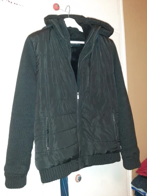 Svart jacka med huva från Firetrap - Säljer en svart jacka från Firetrap i storlek M. Jackan har stickade ärmar, quiltad kropp och mjukt foder. Utrustad med dragkedja, två fickor fram och en skön huva. Perfekt för kyliga dagar och riktigt snygg streetstil.