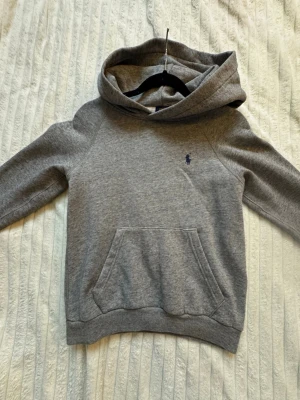 Grå hoodie från Polo Ralph Lauren - Säljer en klassisk grå hoodie från Polo Ralph Lauren i storlek XXS. Hoodien har en stor ficka framtill och ribbade muddar vid ärmslut och nederkant. Perfekt för dig som gillar stilrena basics och vill ha något mjukt och bekvämt.💘