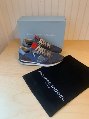 Blå Philippe Model sneakers med röd detalj - Säljer ett par riktigt schyssta Philip model. Har använt dem lite dem är i skick 7,5/10.  Original pris 2500kr säljs nu då för 1500. Skriv om du är intresserad! Är öppen för alla frågor👍