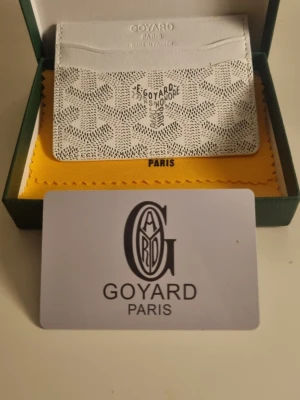 Vit kortfodral från G4yard - Snyggt och exklusivt kortfodral från G4yard i vitt med det klassiska mönstret och logotypen framtill. Tillverkat i läder med flera kortfack och elegant design. Perfekt för dig som vill ha en stilren och lyxig accessoar från Paris.