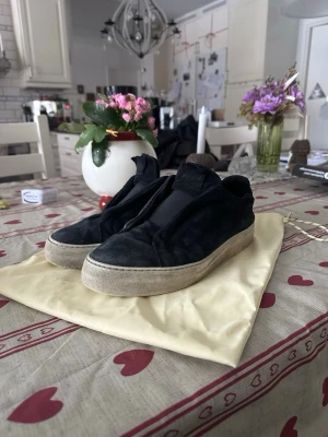 Svarta sneakers från Axel Arigato - Säljer ett par svarta sneakers från Axel Arigato med ovandel i mocka och bred vit sula. Klassisk låg modell utan synliga snören och diskret logga på plösen. Perfekta för dig som gillar stilrena och minimalistiska skor.