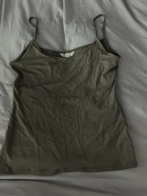 Mörkgrön linnetopp med smala band - En enkel och stilren mörkgrön linnetopp med tunna axelband. Toppen har en rak passform och är tillverkad i mjukt bomullsmaterial, perfekt för varma dagar eller som lager under andra plagg.