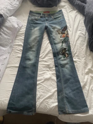 Jeans med brodyr Miss Sixty  - Säljer ett par blå bootcut jeans från Miss Sixty. Några tappade stenar vilket syns på bilden.                          Innerbenslängd:78-79cm.                 Storlek:27