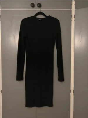 Svart långärmad klänning Urban Classics - En stilren svart långärmad klänning från Urban Classics. Klänningen är figurnära med rund halsringning och enkel design, perfekt att styla med accessoarer. Mjuk och stretchig känsla för en bekväm passform.