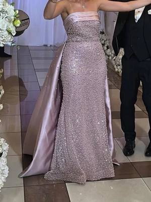 Glittrig ljusrosa balklänning - Elegant axelbandslös långklänning i ljusrosa med glittriga pärlor som flirtar under kvällens gång och släp. Klänningen har en figurnära passform och är perfekt för bal, bröllop eller fest. Klänning kommer med ett borttagbart släp som kan tas bort vid behov. Klänningen är i storlek 36-38 och har bara används en gång. Priset kan diskuteras☺️