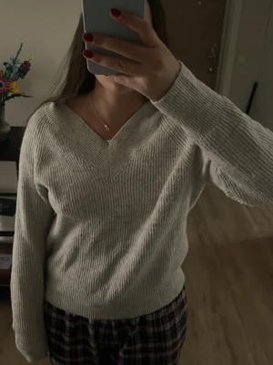 Ljusgrå stickad tröja V-ringad - Ljusgrå stickad tröja från Primark med V-ringning och ribbade muddar. Tröjan har en avslappnad passform och är tillverkad i mjukt material som passar perfekt för kyligare dagar. Enkel och stilren design som är lätt att matcha.