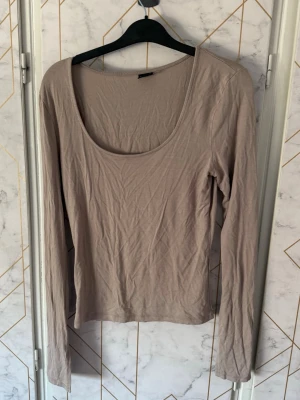 Beige långärmad topp Gina Tricot - En enkel och stilren beige långärmad topp från Gina Tricot. Längst ner på ärmarna har de en slits. Toppen har en djup rundad urringning och är tillverkad i mjuk material. Artikelnummer 16981-2022.