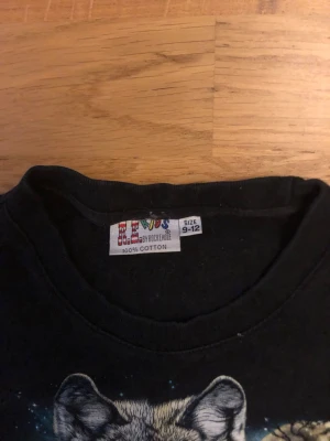 Svart t-shirt med vargmotiv - Svart t-shirt från B.L. Kids by Rock Eagle i 100% bomull. Framsidan har ett stort tryck med vargar som ger en cool och unik vibe. Klassisk passform och rund hals, perfekt för dig som gillar djurmotiv och vill ha något som sticker ut.