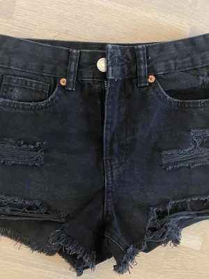Svarta denimshorts med slitningar - Säljer ett par svarta denimshorts från Denim Project med råa kanter och slitna detaljer både fram och bak. Oanvända, priset går att diskuteras