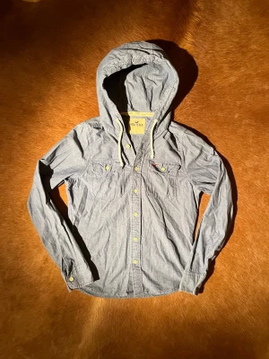 Blå overshirt med huva från Hollister - Tjena! Säljer denna sjukt unika och eftertraktade skjorta med huva från Hollister. Den är sjukt fet och passar perfekt inför våren☀️Den är i L men sitter som en M. Vid minsta fråga eller fundering hör av er🤠