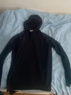 Svart hoodie från RYVLS Stockholm - En svart hoodie från RYVLS Stockholm med klassisk huva och långärmad design. Hoodien har en enkel och stilren look, perfekt för dig som gillar minimalistiskt mode. Materialet känns mjukt och bekvämt mot huden.