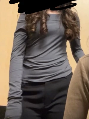 Mörkgrå långärmad offshoulder topp - Snygg mörkgrå långärmad topp med offshoulder-design. Toppens material känns mjukt och stretchigt, perfekt för en stilren look. Passformen är slim och toppen är enfärgad utan mönster eller detaljer.