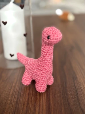 Rosa virkad dinosaurie - Söt handvirkad dinosaurie i rosa garn med svart broderade ögon. Perfekt som dekoration eller leksak. Den har lång hals, liten svans och fyra ben. Mjuk och lätt att hålla i handen.