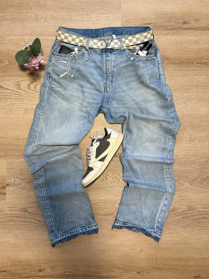 Ljusblå raka jeans med rå kant - Säljer ett par ljusblå jeans med rak passform och rå, fransig kant nedtill. Jeansen har klassisk femficksdesign och är gjorda i denim. Perfekta för en avslappnad och trendig look.