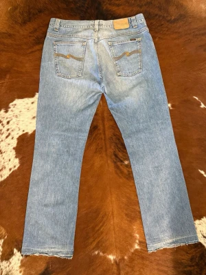 Nudie BootcutOla - Tjena! Säljer dessa sjukt feta Nudie-jeans ifrån tidigt 2000-tal. Mycket bra skick för att vara så pass gamla!  Nypris: på dom liknade modeller som finns nu ligger på 1800-2000kr  Modell-lappen är borta men jag är 99% säker på att modellen är BootcutOla. De passar som en W36 / L34 (Midjan är ca 47 cm platt och ytterbenet är 110 cm).  Hör av dig vid funderingar! 🙌