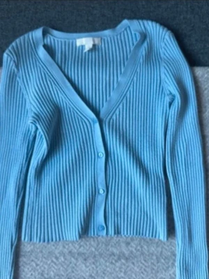 Ljusblå ribbad kofta från H&M - Säljer en ljusblå ribbad kofta från H&M med v-ringning och långa ärmar. Koftan är lite nopprig men annars i bra skick!