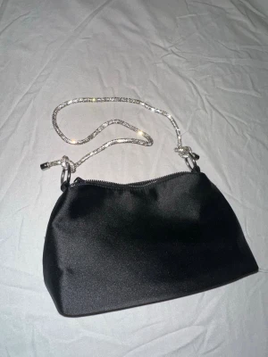 Handväska - Simpel svart handväska med elegant glittrig ”band”. köpt på primark många år sedan men inte riktigt använt alls 