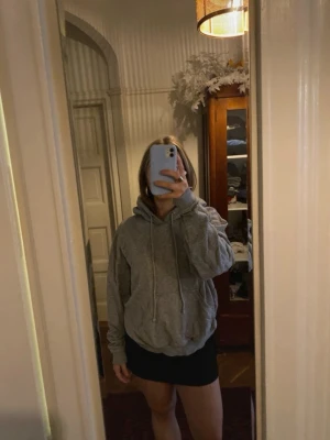 Grå hoodie med huva och ficka - En klassisk grå hoodie med stor huva och dragsnören. Hoodien har en rymlig passform, magficka och ribbade muddar vid ärmar och nederkant. Perfekt för en chill och avslappnad stil. Materialet känns mjukt och bekvämt.