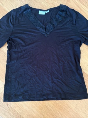 Svart topp med spetsdetaljer Gina Tricot 170 - Svart topp med långa ärmar och  V-ringning dekorerad med bred spetskant. Från Gina Tricot i storlek 170