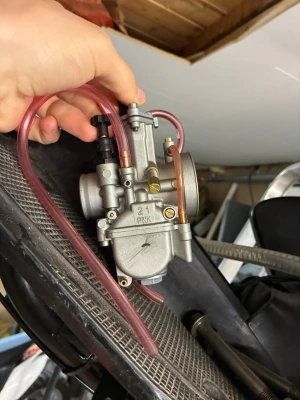 21mm förgasare med slangar - Säljer en 21mm förgasare i metall med rosa bränsleslangar och justerskruv. Passar till moped eller mindre motorcykel. Märkt med '21 PWK' på sidan. Perfekt för dig som vill trimma eller byta ut din gamla förgasare.