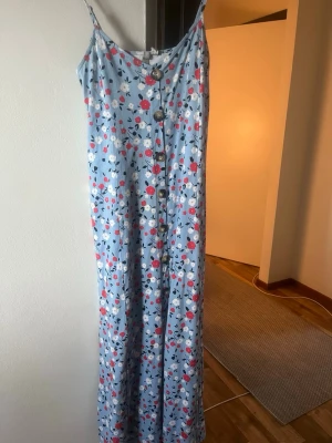 Klänningar, strl 36 - Säljer två fina långklänningar. Ena är ljusblå med blommigt mönster, smala axelband och knappar framtill. Den andra är ljusblå från Pieces, med v-ringning, korta puffärmar och broderade detaljer. Perfekta för varma dagar!