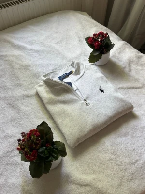 Vit halvzip från Polo Ralph Lauren - Snygg vit halvzip-tröja från Polo Ralph Lauren med klassisk broderad logga på bröstet. Tröjan har hög krage och dragkedja framtill, perfekt för en clean och stilren look. Tillverkad i mjukt material som känns skönt mot huden.
