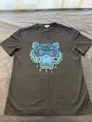 Svart Kenzo t-shirt - Kenzo t-shirt i svart med ikoniskt tigertryck i blått och grönt på bröstet samt texten 'KENZO PARIS'. Klassisk rund hals och korta ärmar. Tillverkad i mjuk bomull för en skön känsla och snygg passform.