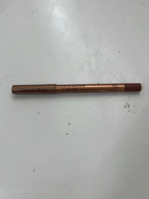 Charlotte Tilbury Iconic Nude läppenna - Läppenna från Charlotte Tilbury i färgen Iconic Nude. Pennan har en mjuk, krämig formula och kommer i en snygg guldbrons-färgad hylsa med matchande lock. Perfekt för att definiera och forma läpparna med en naturlig nude-ton.