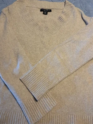 Beige stickad tröja - Mysig beige stickad tröja från New yorker med V-ringning och breda ribbade muddar vid ärmslut och nederkant. Tröjan har en enkel och stilren design, perfekt för lager på lager och passar till det mesta. Materialet känns mjukt och bekvämt.