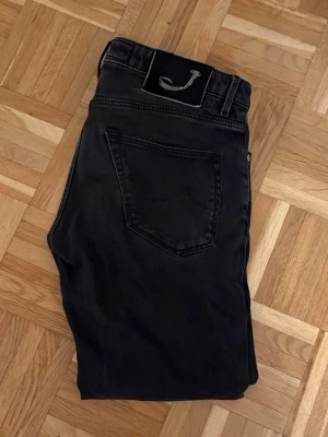 Svarta jeans från Jacob Cohën - Snygga svarta jeans från Jacob Cohën med klassisk femficksmodell och raka ben. Jeansen har en diskret logga på bakfickan och patch med broderad J på linningen. Tillverkade i mjukt denimtyg som ger en skön passform.