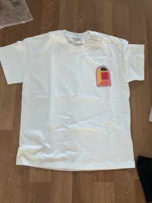Vit Casa Blanca t-shirt med färgglatt tryck - Säljer en vit t-shirt från Casa Blanca med ett stort färgglatt grafiskt tryck i rosa, gul, röd och svart på bröstet och ryggen. T-shirten har klassisk passform och rund hals. Perfekt för dig som gillar stilrena plagg med en twist. Kan gå ner i pris vid snabb affär 
