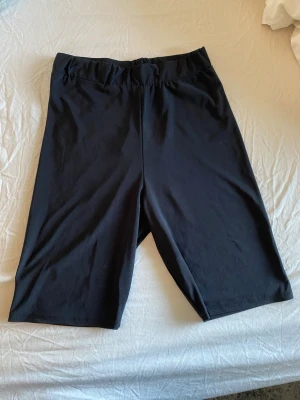 Svarta cykelshorts i stretchigt material - Säljer ett par svarta cykelshorts med elastisk midja och tight passform. Shortsen är tillverkade i ett stretchigt syntetmaterial som passar perfekt till träning eller en aktiv vardag. Klassisk och enkel design utan synliga detaljer.