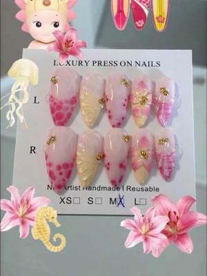 Lyxiga rosa press-on naglar med 3D-design - Handgjorda press-on naglar i mixad rosa och nude färg med 3D-blommor, gulddetaljer och olika mönster. Naglarna har en spetsig almondform och kommer i storlek M. Perfekt för dig som vill ha unika och kreativa naglar med lyxig känsla.