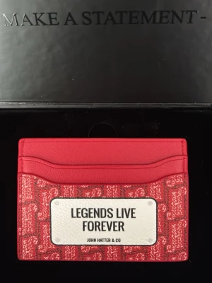 Röd korthållare John Hatter & Co - Snygg röd korthållare från John Hatter & Co i läder med vit patch framtill där det står 'Legends Live Forever'. Korthållaren har flera fack för kort och ett coolt mönster i rött och vitt. Perfekt accessoar för dig som vill sticka ut. Pris kan diskuteras vid snabb affär 