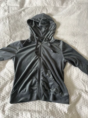 Grå zip hoodie i mjuk velour - Säljer en grå hoodie i mjuk velour med dragkedja framtill och två fickor. Tröjan har huva med dragsko och långa ärmar. Perfekt för en chill och avslappnad stil.