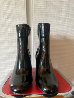 Svarta lackade stövletter med klack - Snygga svarta stövletter i glansigt lackmaterial med rundad tå och bred klack. Dragkedja på insidan för enkel på- och avtagning. Perfekta för dig som vill ha en edgy och trendig look.