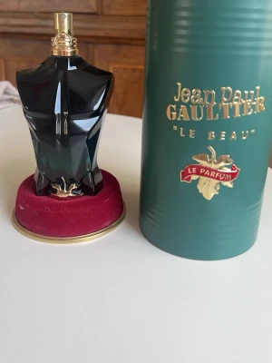 Jean Paul Gaultier Le Beau Le Parfum ca 110 ml kvar - Unik parfymflaska formad som en manlig torso i svart och guld från Jean Paul Gaultier, modellen Le Beau Le Parfum. Flaskan har en elegant och lyxig design med gulddetaljer och levereras med original grön förpackning med guldfärgad text.