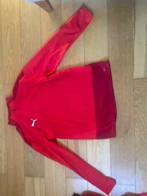 Röd träningsjacka från Puma - Snygg röd träningsjacka från Puma med dragkedja framtill och klassisk vit Puma-logga på bröstet. 