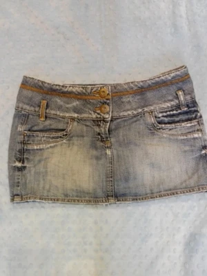 Kort jeanskjol med slitningar - Snygg kort jeanskjol i ljusblå denim med slitna detaljer och dubbla knappar framtill. Zaras märke TRF