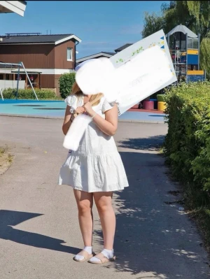 Vit kortklänning med volang och knyt - Söt vit kortklänning med volangdetaljer och v-ringning. Klänningen har korta ärmar och knytband i nacken. Tillverkad i ett lätt bomullsliknande material med diskret struktur. Perfekt för sommarens alla tillfällen.
