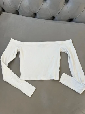 Vit offshoulder topp från Bik Bok - Trendig vit offshoulder topp från Bik Bok i ribbad bomull. Croppad modell med långa ärmar och smal passform som sitter snyggt på kroppen. Perfekt att styla med höga jeans eller kjol för en clean look.