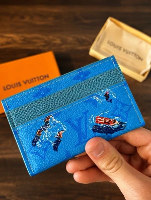 Blå Louis Vuitton kortfodral - Snyggt blått kortfodral från Louis Vuitton med lekfullt tryck av simmande personer och en röd båt. Tillverkat i tåligt läder med diskret LV-monogram i bakgrunden. Perfekt för kort och ID, smidig att ha i fickan. Lyxig och unik accessoar för dig som gillar färg.