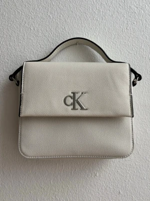 Calvin Klein väska - minimal monogram boxy flap - Vit handväska/crossbody väska från Calvin Klein. Väskan är använd ett fåtal gånger och är i mycket bra skick. Minimal monogram boxy flap. 