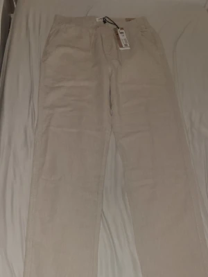 Beiga linnebyxor från Lindex - Snygga och luftiga beiga linnebyxor från Lindex med dragsko i midjan och raka ben. Byxorna har sidofickor och är perfekta för en chill och stilren look. Materialet är linneblandning som känns skönt mot huden.